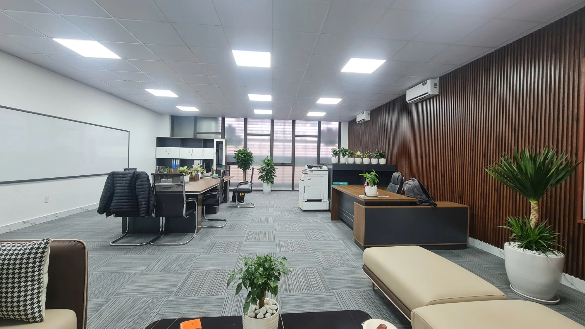 Khu làm việc chung với bàn gỗ, máy in và sofa tiếp khách