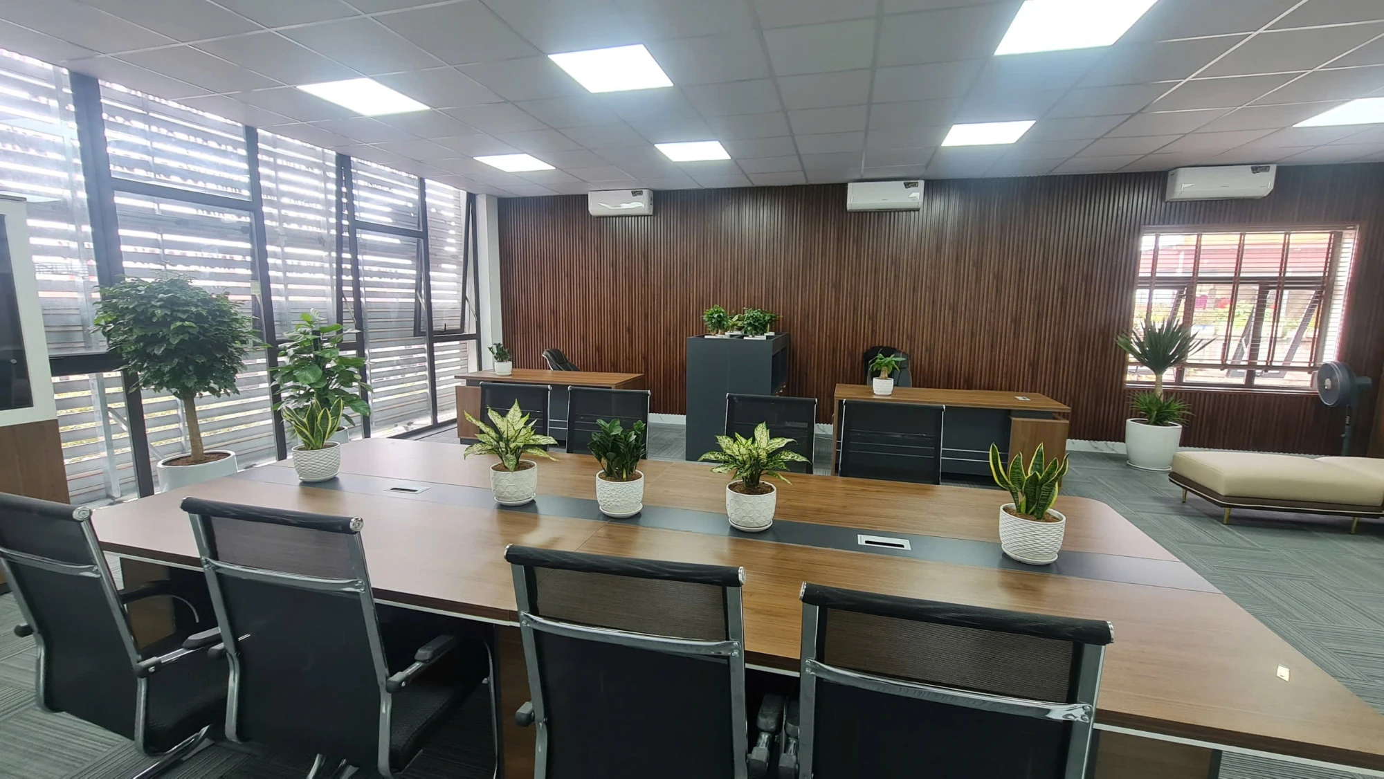 Phòng họp lớn với bàn dài, ghế lưới và cây xanh